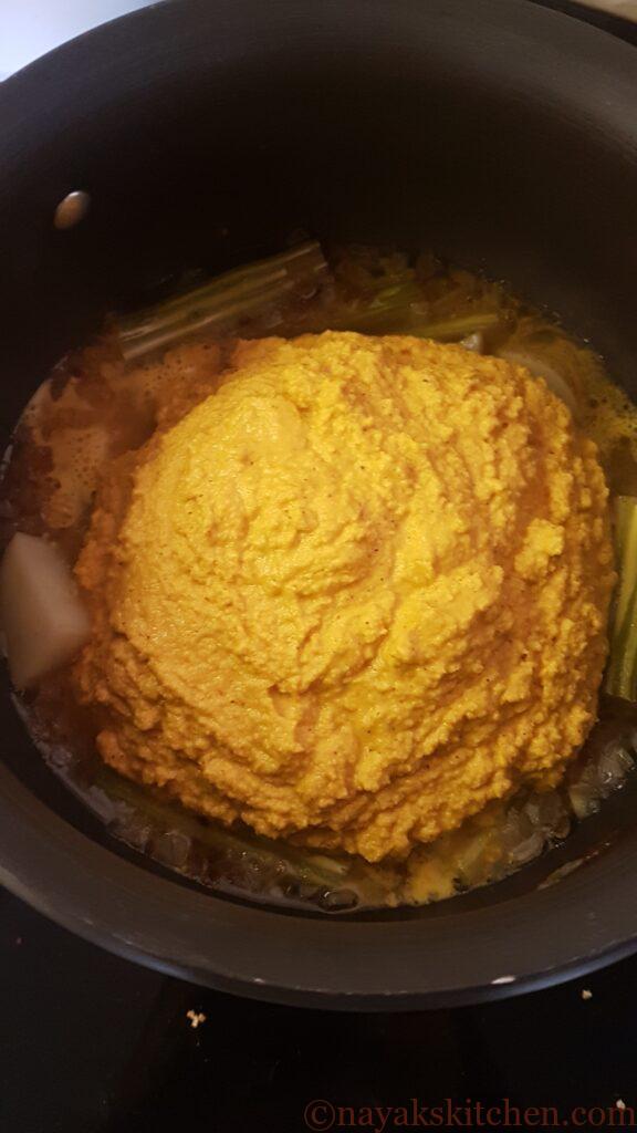 Adding ground paste to cooked drumsticks and potatoes